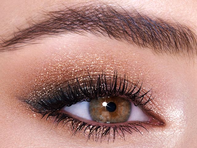 Single-eye close-up of a fair-tone model with hazel eyes wearing shimmery gold and brown eyeshadow. 