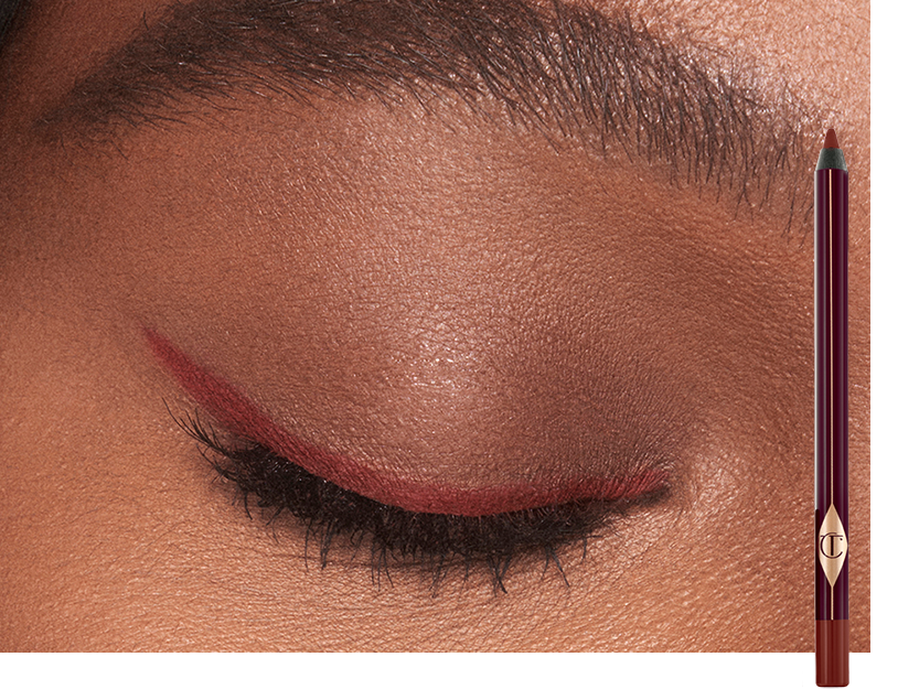 Single-eye close-up of a deep-tone model wearing a berry-rose eyeliner in a soft wing style with the eyeliner pencil next to her.