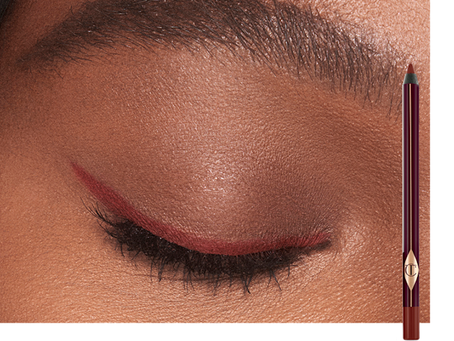 Single-eye close-up of a deep-tone model wearing a berry-rose eyeliner in a soft wing style with the eyeliner pencil next to her.