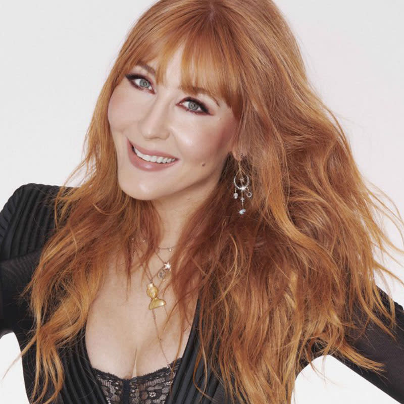 A portrait of Charlotte Tilbury wearing dewy, nude pink makeup with dangling earrings and chain necklaces. 