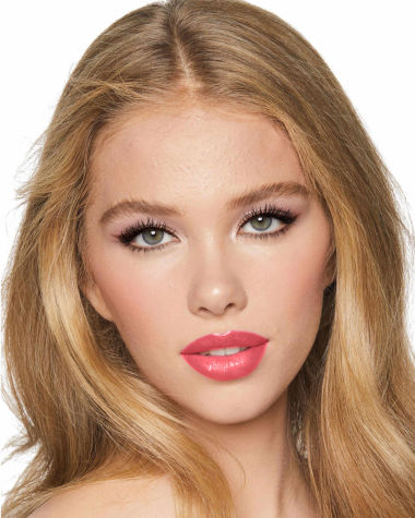 A light-tone model with green eyes wearing shimmery rose gold and brown eye makeup with brown eyeliner, soft pink blush, and coral-pink lipstick with gloss on top. 