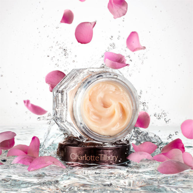 Magic Night Cream open banner Banner with an open glass jar with thick, peach-coloured night cream and its dark-brown and gold-coloured lid placed on top of crystal-clear water with rose petals falling down on it.
