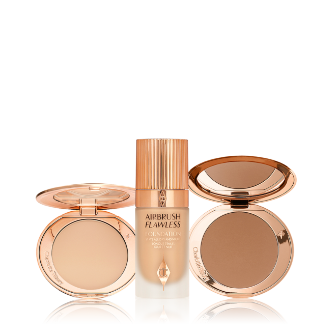 An open, mirrored-lid bronzer compact, medium-tone foundation in a frosted glass bottle with a rose-gold lid, and a mirrored-lid deep-tone pressed powder compact. 