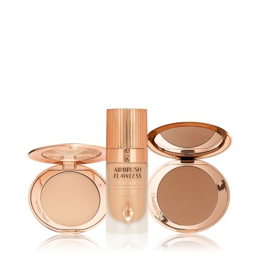 An open, mirrored-lid bronzer compact, medium-tone foundation in a frosted glass bottle with a rose-gold lid, and a mirrored-lid deep-tone pressed powder compact. 