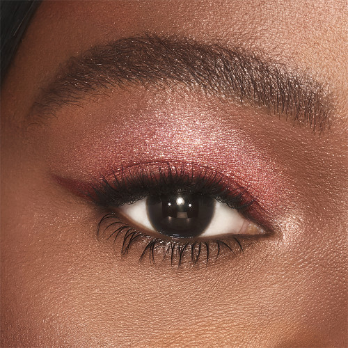 Single-eye close-up of a deep-tone model with brown eyes wearing shimmery berry-pink eyeshadow.