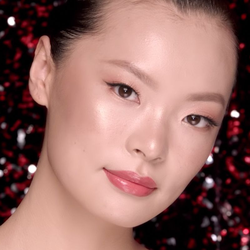 A fair-tone model with brown eyes wearing soft rose-gold eye makeup with coral lip gloss. 
