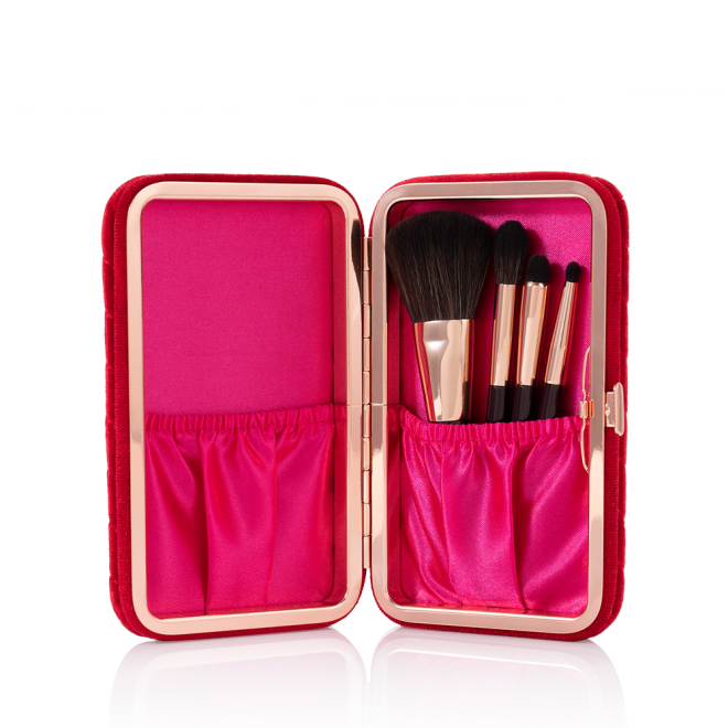 An open, bright-fuchsia-coloured velvet brush clutch with travel-sized face and eyeshadow brushes inside.