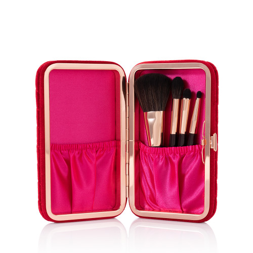 An open, bright-fuchsia-coloured velvet brush clutch with travel-sized face and eyeshadow brushes inside.