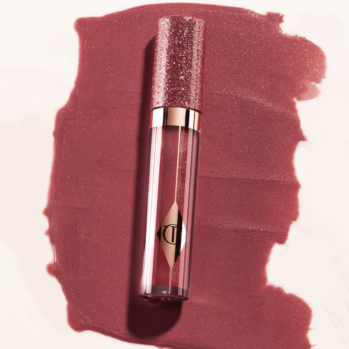 A berry-pink lip gloss in a glass tube with a shimmery strawberry-red lid placed on its swatch.