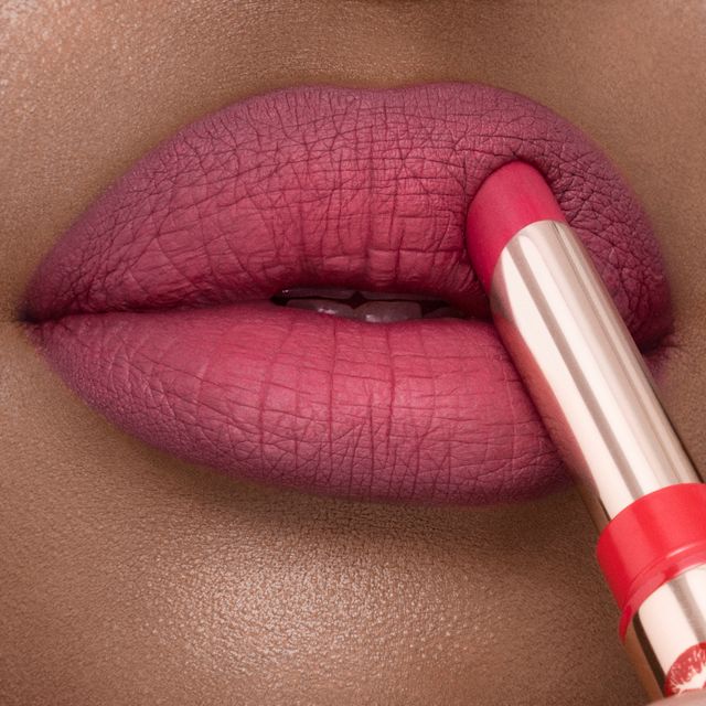 Lips close-up of a deep-tone model wearing a soft pink-red lipstick with a matte finish.