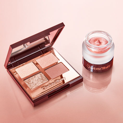 An open, mirrored-lid quad eyeshadow palette in shades of pink, gold, and brown with cream eyeshadow in a glass pot in a rose gold shade.