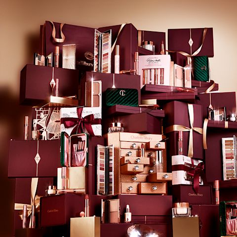A collection of makeup and skincare items packed in dark crimson gift boxes with ribbons. 