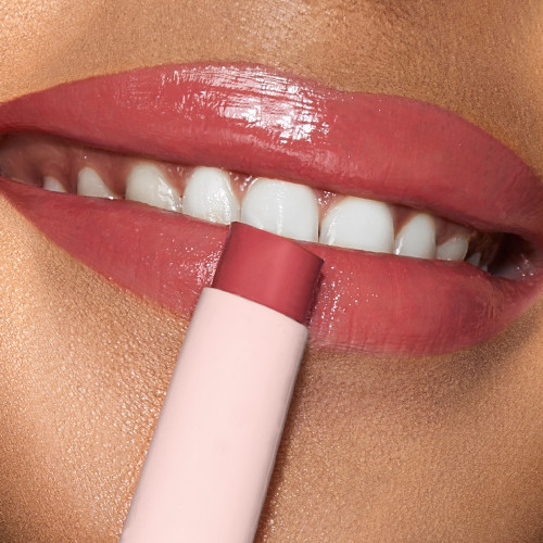 Lips close-up of a medium-tone model applying a moisturising lipstick balm in a cherry-red shade. shade.