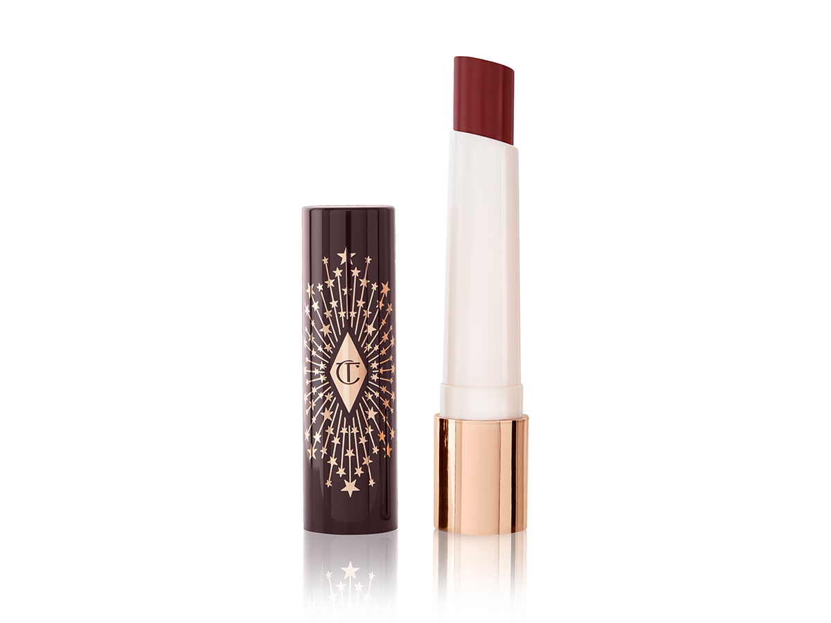 An open lipstick lip balm in a berry shade, in white and gold tube with a black-coloured lid with gold sparkles all over it.