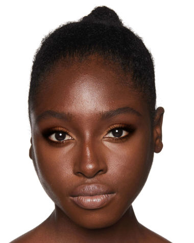 A deep-tone model with brown eyes wearing nude pink lipstick with matte eye makeup in shades of light brown, dark brown, and peach. 