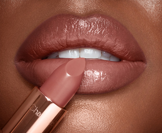 Lips close-up of a deep-tone model applying lipstick in a soft rosy peach shade with a satin finish.