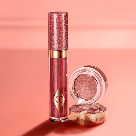 A peach-toned banner with a shimmery berry-pink lip gloss in a glass tube with a glittery lid next to shimmery, cream eyeshadow in a berry-pink shade in a glass pot with its lid removed.
