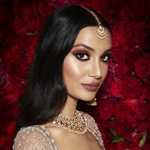 Mannequin à la peau médium et aux yeux marron portant un fond de teint éclatant avec un fard à joues terracotta discret, un rouge à lèvres rose framboise foncé, un trait de crayon kohl et un maquillage des yeux brun-prune charbonneux. 