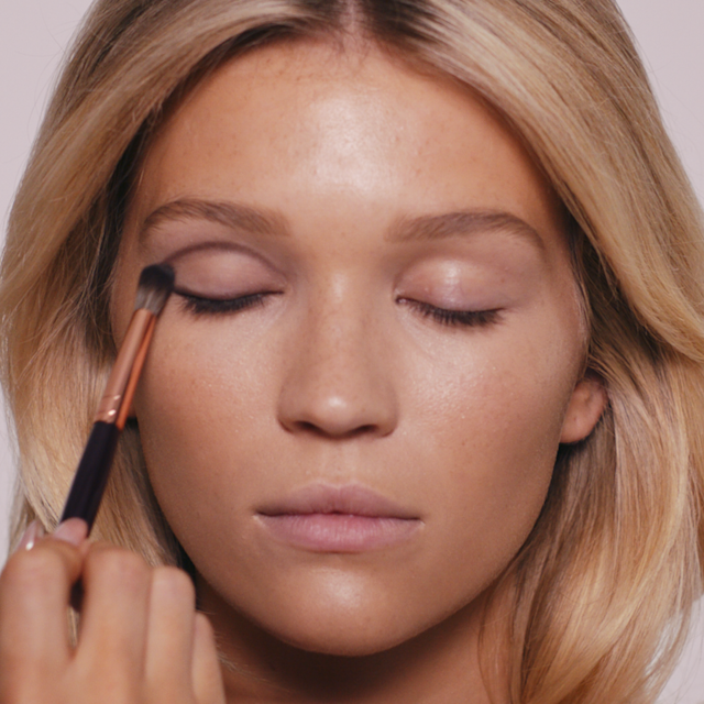 Fair blonde model with eyes closed having a nude matte eyeshadow being applied to her eyelid.