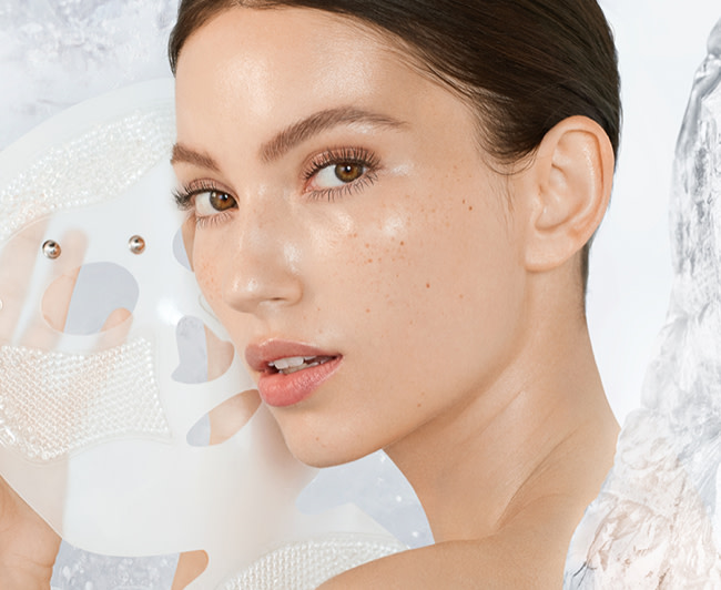 Fair-tone brunette model removing a reusable, white-coloured mask, revealing glowy, flawless, and lifted skin. 