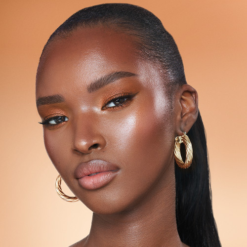 Deep-tone brunette model with brown eyes wearing shimmery bronze eyeshadow with black eyeliner, nude rose matte lipstick with nude rose blush, and glowy opal-coloured highlighter for a flawless, glowy look.