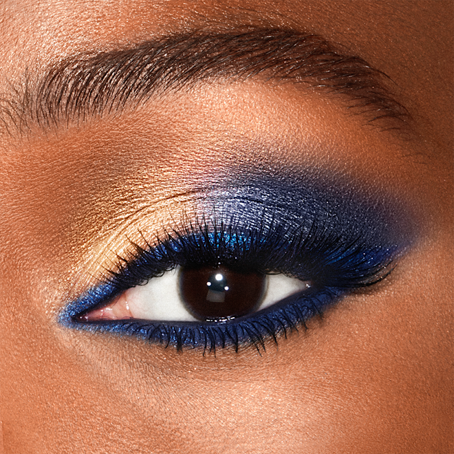 Luxury Palette Eyeshadow in Super Blue eye makeup close-up Close-up of a shimmery, royal-blue and golden eye look on a deep-tone model with dark brown eyes.