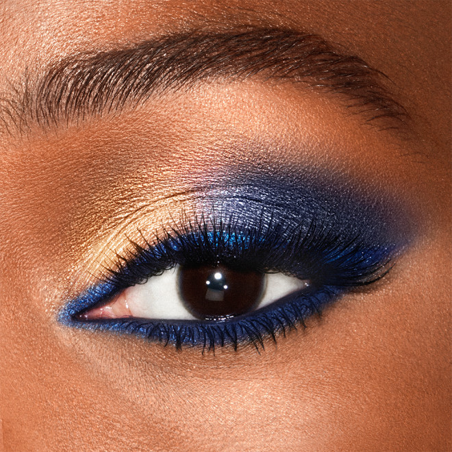 Close-up of a shimmery, royal-blue and golden eye look on a deep-tone model with dark brown eyes.