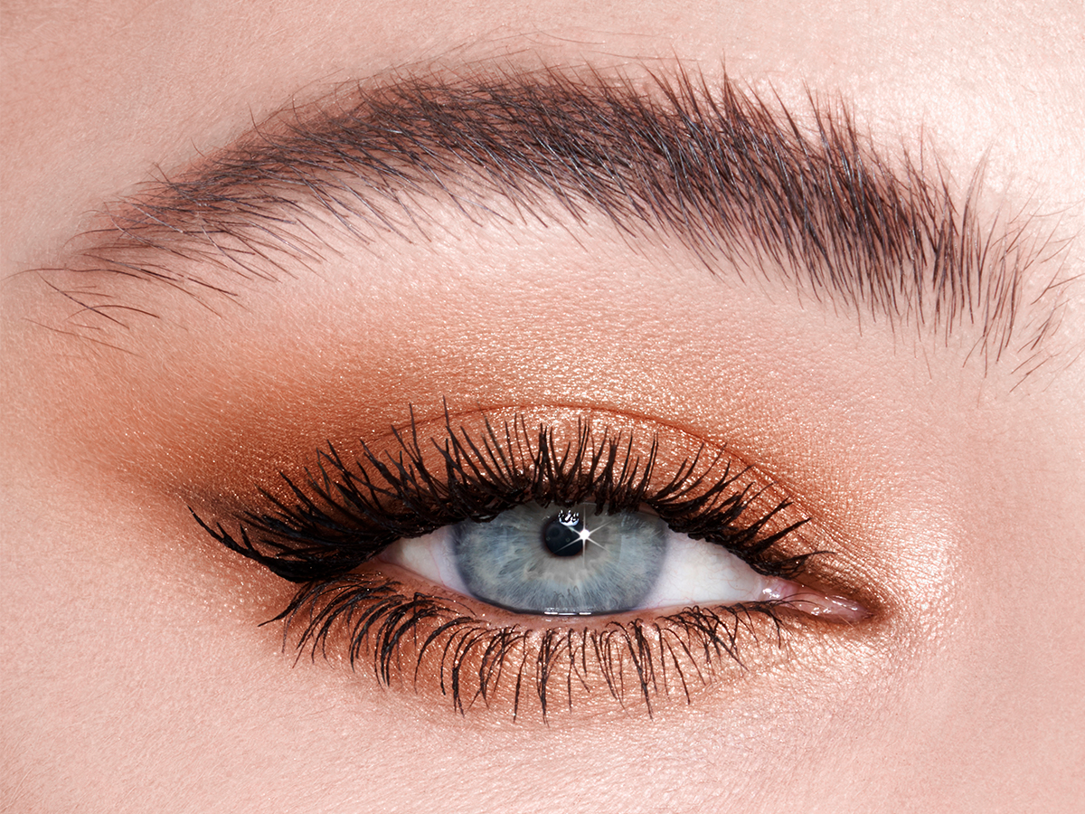 Single eye close-up of a fair-tone model with blue eyes wearing shimmery topaz eye makeup. 