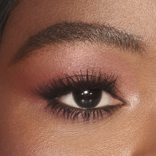 Single-eye close-up of a brown-eyed deep-tone model wearing shimmery berry-pink eye makeup.