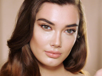 A fair-tone, brunette model with extremely glowy skin, wearing nude-pink gloss and smokey eyeliner. 