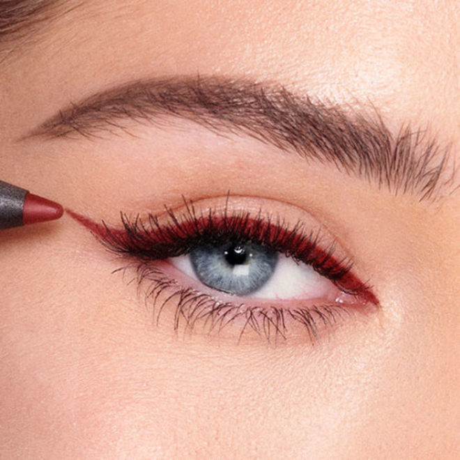 Walk of No Shame Eyeliner on fair-tone model with blue eyes close-up Single-eye close-up of a fair-tone model with blue eyes applying a dark copper-coloured eyeliner pencil in a wing style