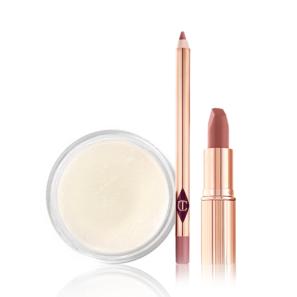 An open lip liner pencil in a nude pink shade, nude pink lipstick with its lid removed, and a white-coloured lip scrub in an open glass jar. 