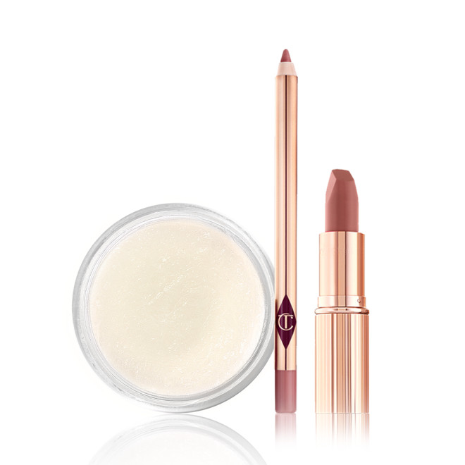 An open lip liner pencil in a nude pink shade, nude pink lipstick with its lid removed, and a white-coloured lip scrub in an open glass jar. 