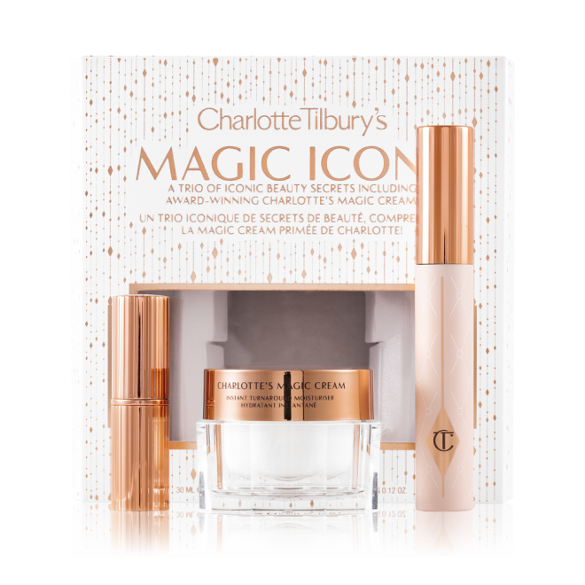 Pearly-white face cream in a glass jar with a gold-coloured lid, black mascara in a pink tube with a gold-coloured lid, and matte lipstick in a gold-coloured tube with their white-coloured packaging box behind them with the text, 'Charlotte Tilbury's Magic Icons' written on it in reflective, gold colour. 