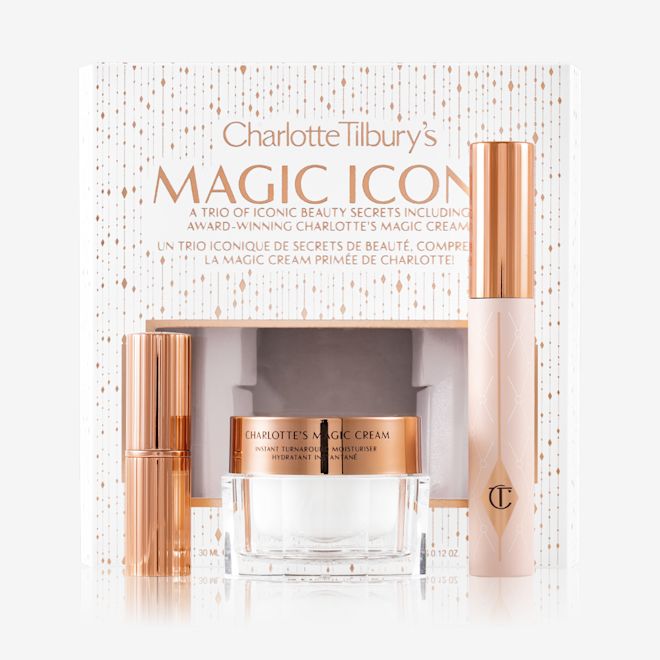 Charlotte Tilbury's Magic Icons kit with box displayed Pearly-white face cream in a glass jar with a gold-coloured lid, black mascara in a pink tube with a gold-coloured lid, and matte lipstick in a gold-coloured tube with their white-coloured packaging box behind them with the text, 'Charlotte Tilbury's Magic Icons' written on it in reflective, gold colour.