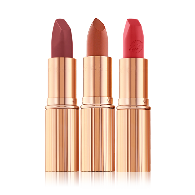 Three open lipsticks in shades of plum, nude terracotta, and fire engine red, in gold-coloured tubes.