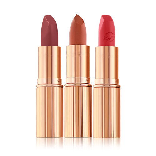 Three open lipsticks in shades of plum, nude terracotta, and fire engine red, in gold-coloured tubes.