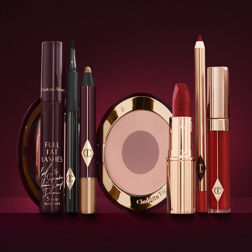 An open two-tone blush in cool-toned pink and brown with a mascara, eyeliner pen, chubby eyeshadow stick in gold, an open lipstick in bold red, lip liner pencil in blood-red, and a lip gloss in bright red. 
