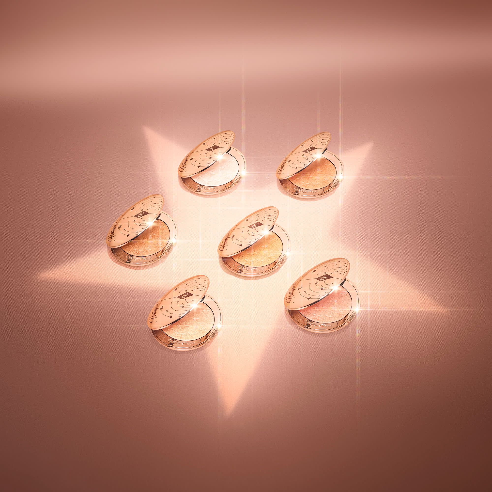 A collection of open, powder highlighter compacts in shades of gold, brown, pink, and silver in sleek, golden-coloured lids.