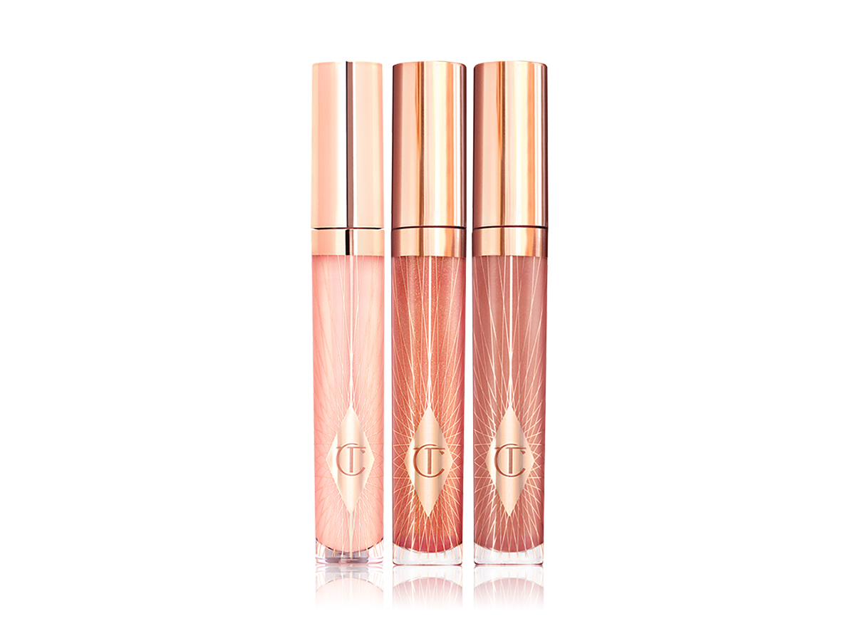 A trio of lip glosses in glass tubes with gold-coloured lids in sheer pink, nude pink, and berry-pink.