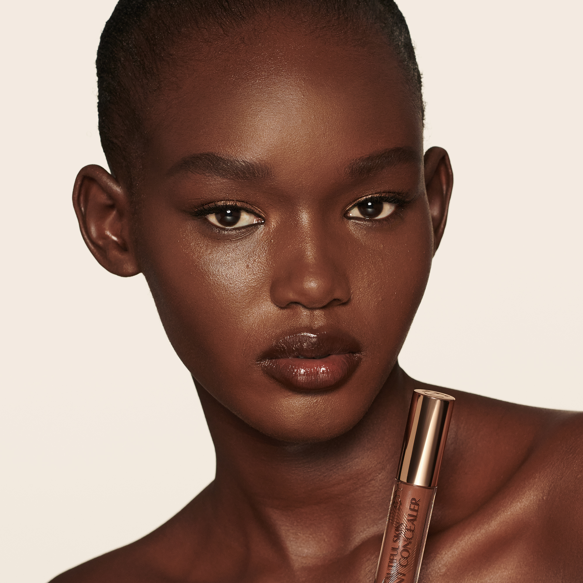 Deep-tone model with brown eyes wearing a radiant, concealer that brightens, covers blemishes, and makes her skin look fresh along with nude lip gloss and subtle eye makeup.