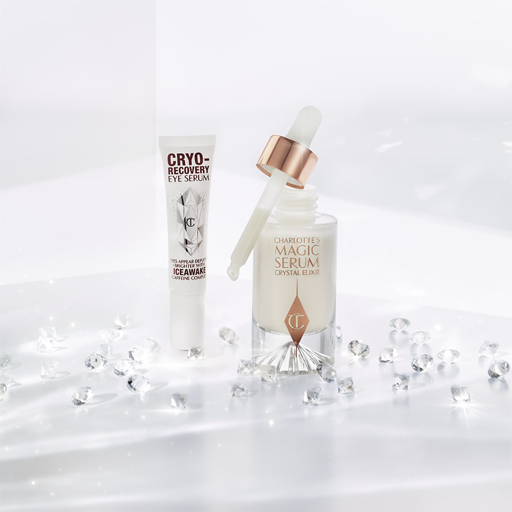 Eye serum in a white-coloured tube with geometric patterns on the front in a reflective, silver colour along with luminous, facial serum in a glass bottle with a white and gold dropper lid.