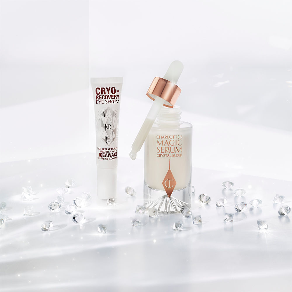 Eye serum in a white-coloured tube with geometric patterns on the front in a reflective, silver colour along with luminous, facial serum in a glass bottle with a white and gold dropper lid.