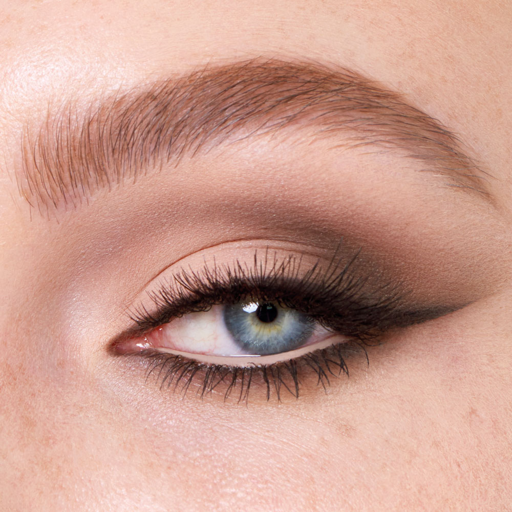 Single-eye close-up of a fair-tone model with blue eyes wearing smokey brown eye makeup with black smoked-out eyeliner.