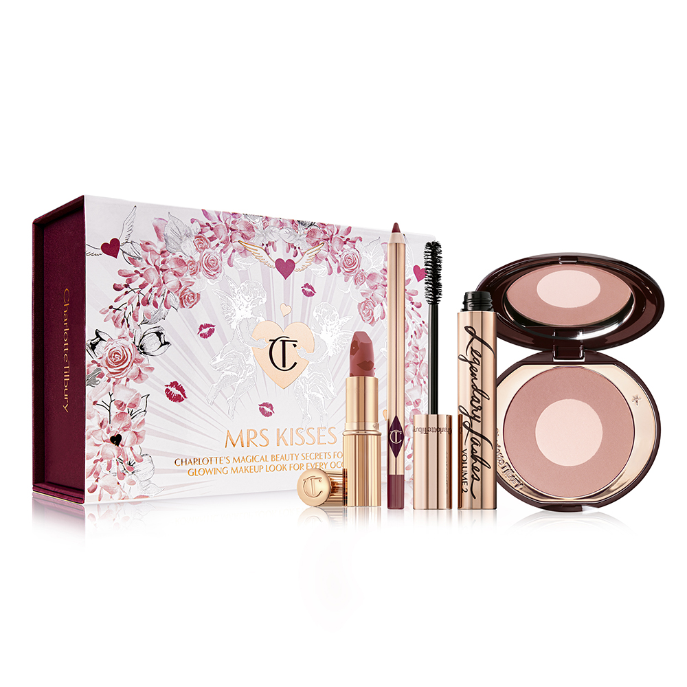 An open brown-red lipstick with a maroon lip liner pencil, an open mascara in golden-coloured packaging, and an open two-tone blush in rose gold and light pink with a white-coloured gift box with hearts and lipstick kiss prints all over with the text, 'Mrs Kisses' written on the front. 