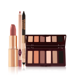 An open matte lipstick in a gold-coloured tube, lip liner pencil, double-ended eyeliner pencil in black and nude beige shades, and an open, mirrored-lid six-pan eyeshadow palette with matte eyeshadows in brown, peach, and beige shades.