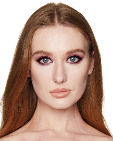 A fair-tone model with auburn hair and blue eyes wearing shimmery maroon, copper, and gold eye makeup along with plum eyeliner. 