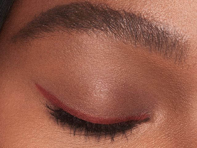 Single-eye close-up of a deep-tone model with eyes closed wearing a dark copper-coloured eyeliner pencil in a soft wing style