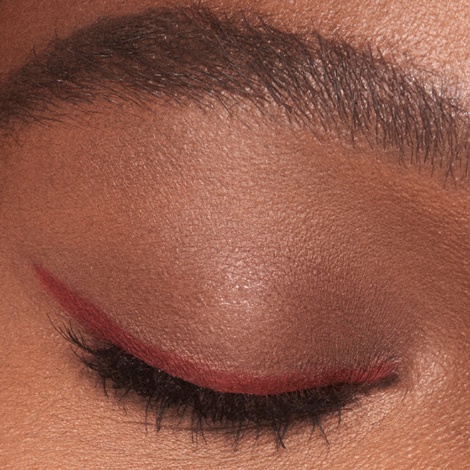 Single-eye close-up of a deep-tone model with eyes closed wearing a dark copper-coloured eyeliner pencil in a soft wing style