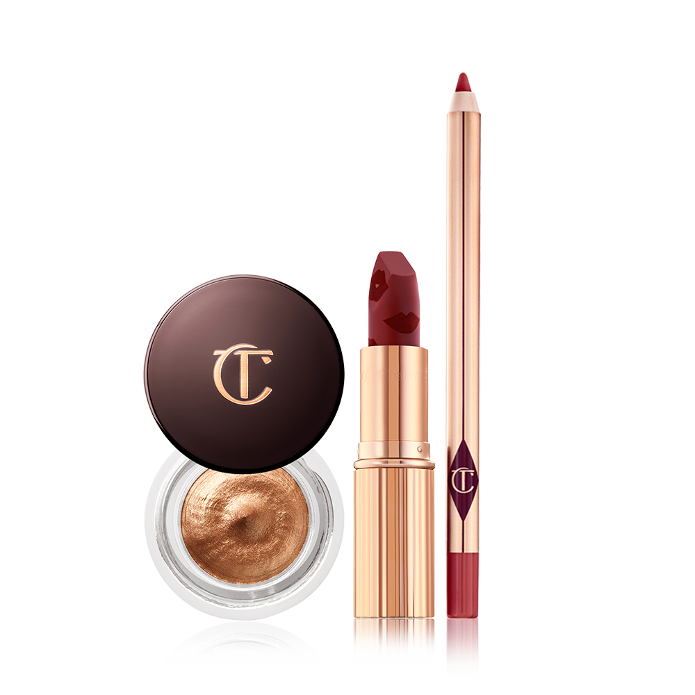 An open matte lipstick in a winter berry shade, lip liner pencil in a berry rose pink shade, and cream eyeshadow in a glass pot in an amber gold shade.